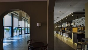 A modern interior with a dining area, a bar, and a large arched doorway leading to a bright space. - Hospedium Hotel Cortijo Santa Cruz (Villanueva de la Serena)