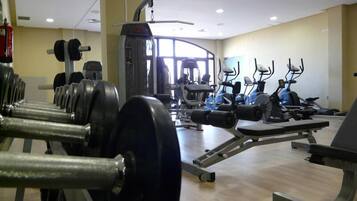 Un gimnasio con diversos equipos de ejercicio, incluyendo mancuernas, una cinta de correr y bicicletas estáticas.