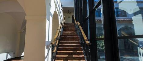 Una escalera de madera con barandillas negras que conduce a un balcón con ventanas grandes.