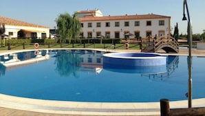 A swimming pool with a bridge, a building with a tiled roof, and a clear sky. - Hospedium Hotel Cortijo Santa Cruz (Villanueva de la Serena)
