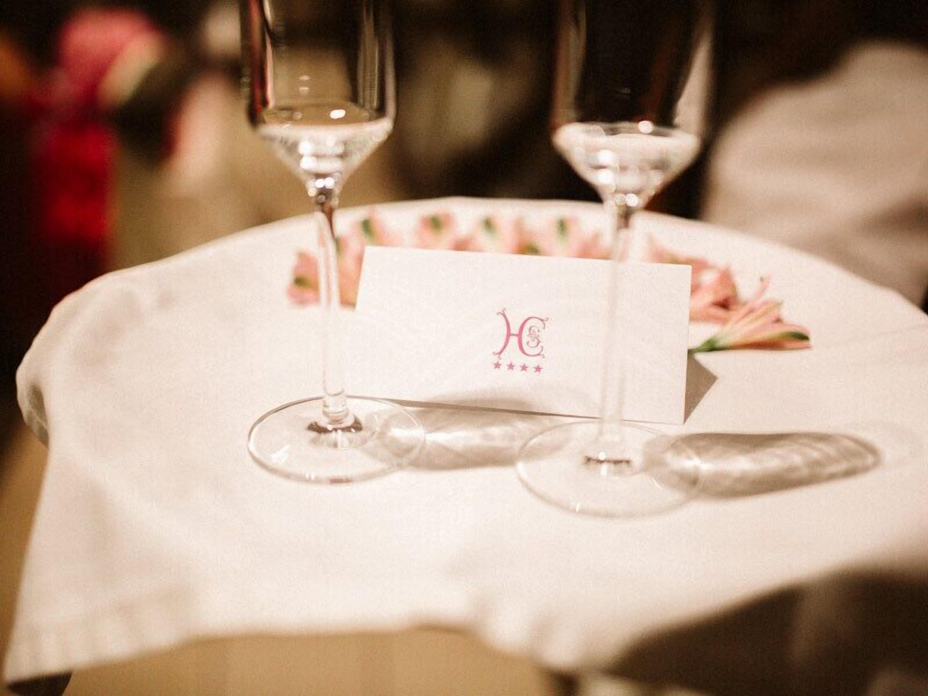 Una mesa con mantel blanco, dos copas de vino y una tarjeta con un logotipo.