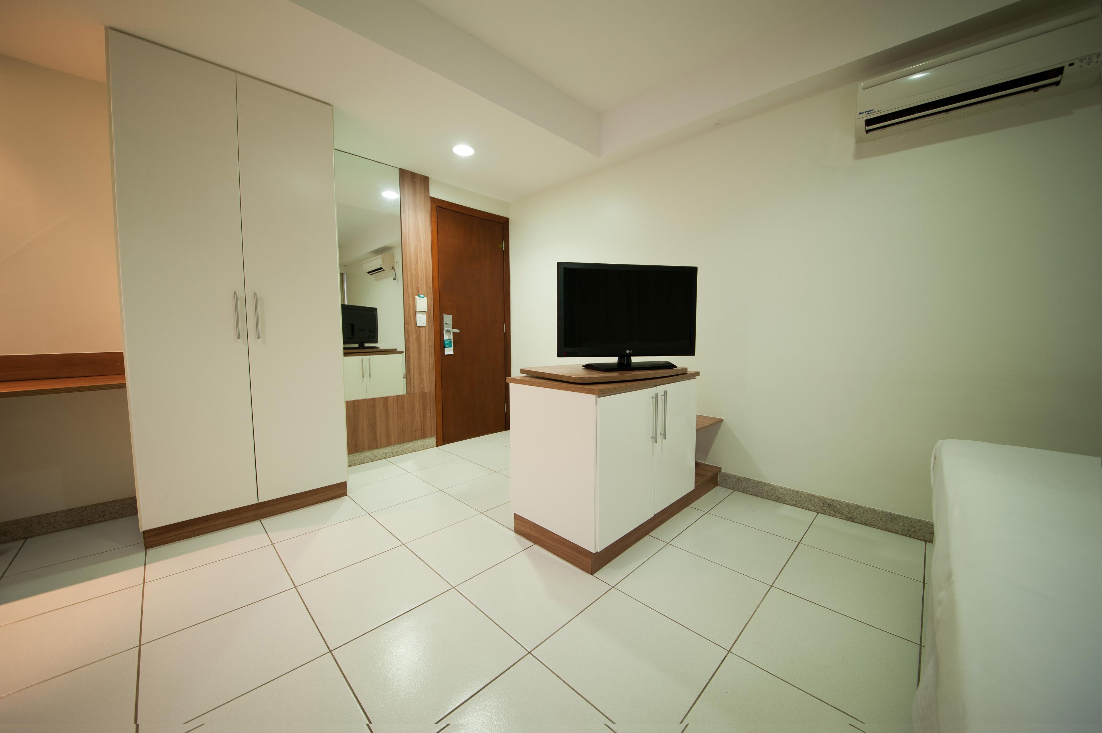 Una habitación con televisión sobre un mueble, un armario y una puerta que da a otra estancia.