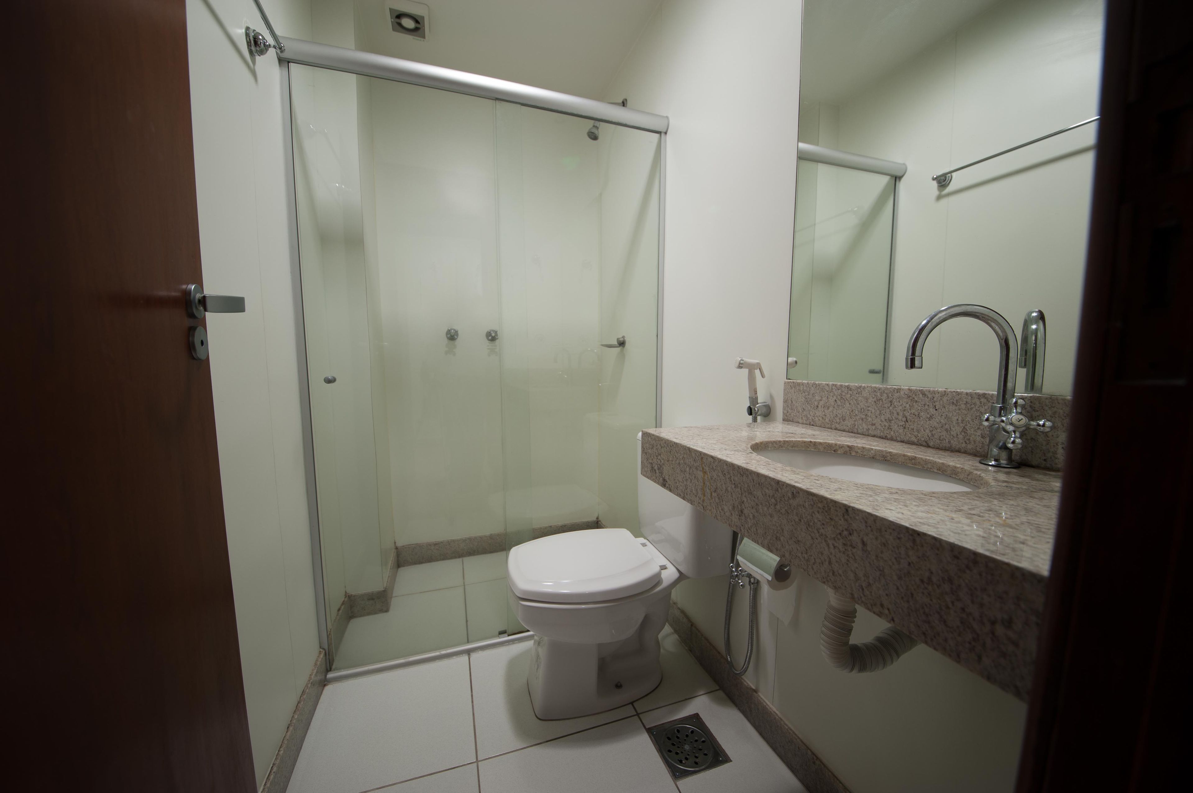 A bathroom with a glass shower enclosure, a toilet, and a sink with a mirror above it.