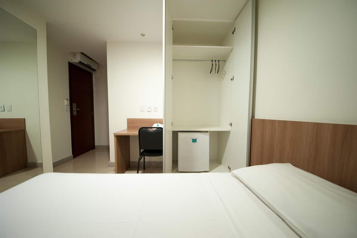 A hotel room with a bed, a desk, a chair, a small refrigerator, and a wardrobe.