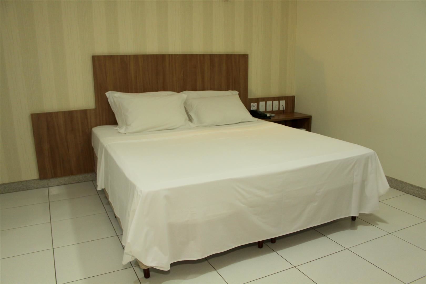 A neatly made bed with white linens, a wooden headboard, and a bedside table with a phone and a lamp.