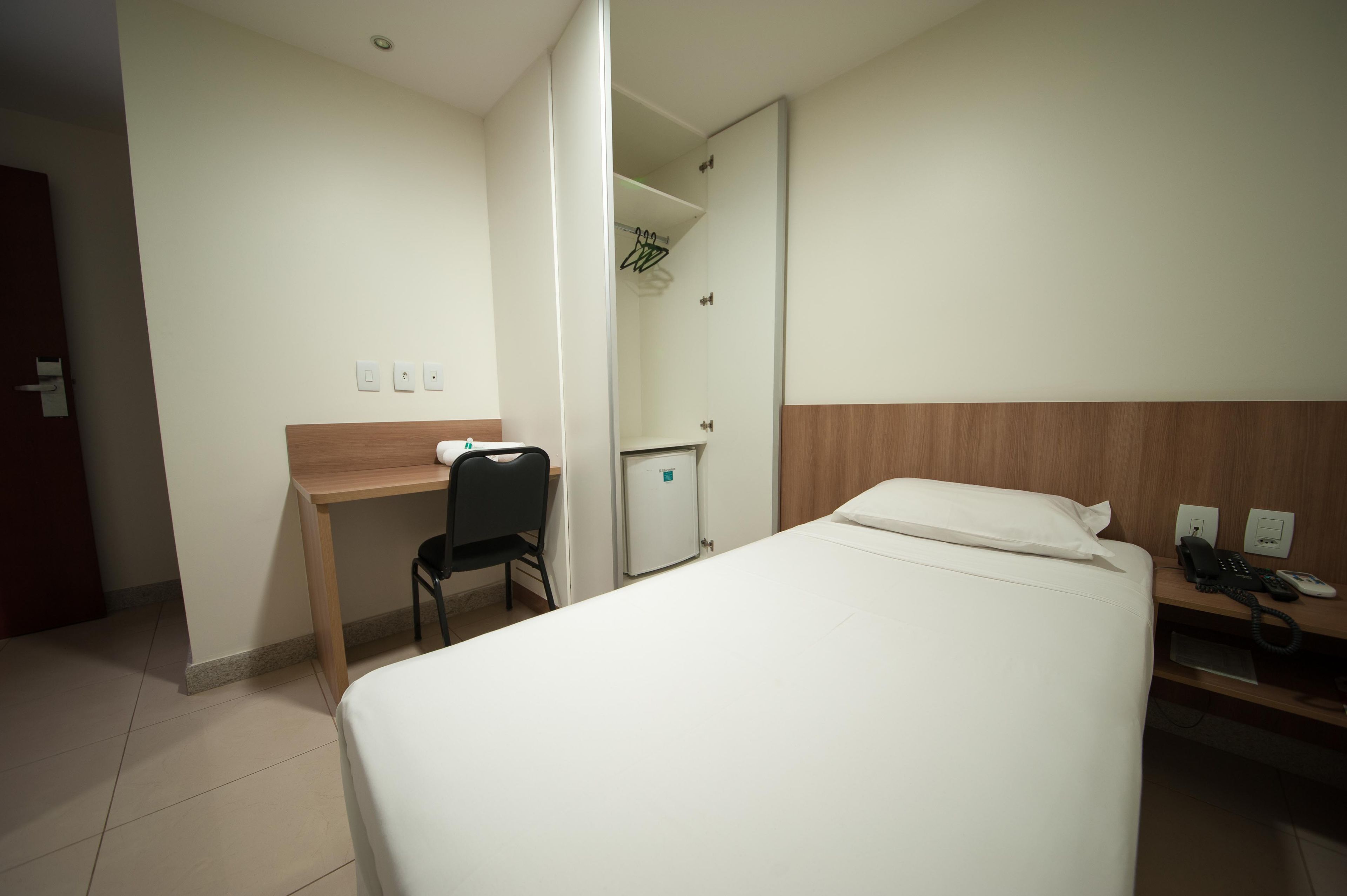 Una habitación de hotel con cama, escritorio, silla, armario y baño pequeño.