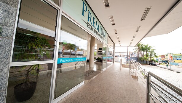 The exterior of a hotel with a glass facade, a sign reading "Premium Executive Hotel," and a covered walkway with a metal railing. - Premium Executive Hotel (Itabira)