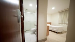 A modern hotel room with a wooden door, a shower area, a toilet, a sink, and a bed. - Premium Executive Hotel (Itabira)