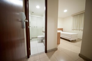 Quarto de hotel moderno com porta de madeira, área de chuveiro, vaso sanitário, pia e cama.