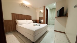 A hotel room with a large bed, a TV on a shelf, and a mirror on the wall. - Premium Executive Hotel (Itabira)