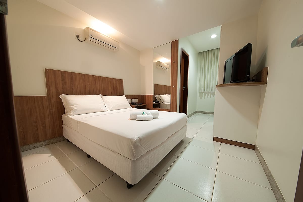 A hotel room with a large bed, a TV on a shelf, and a mirror on the wall.