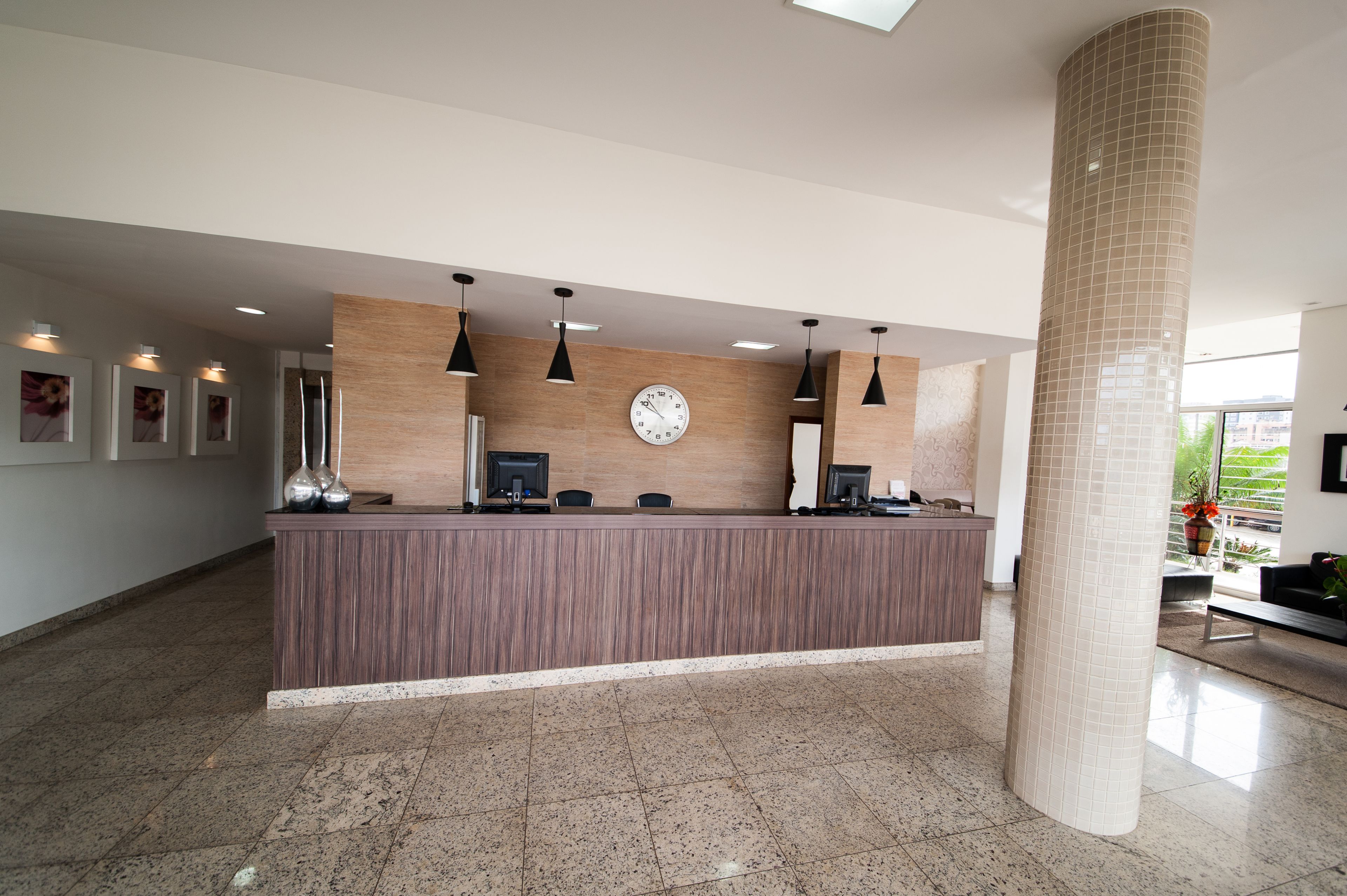 A reception area with a wooden reception desk, multiple computer monitors, pendant lighting, a clock, and a large pillar.
