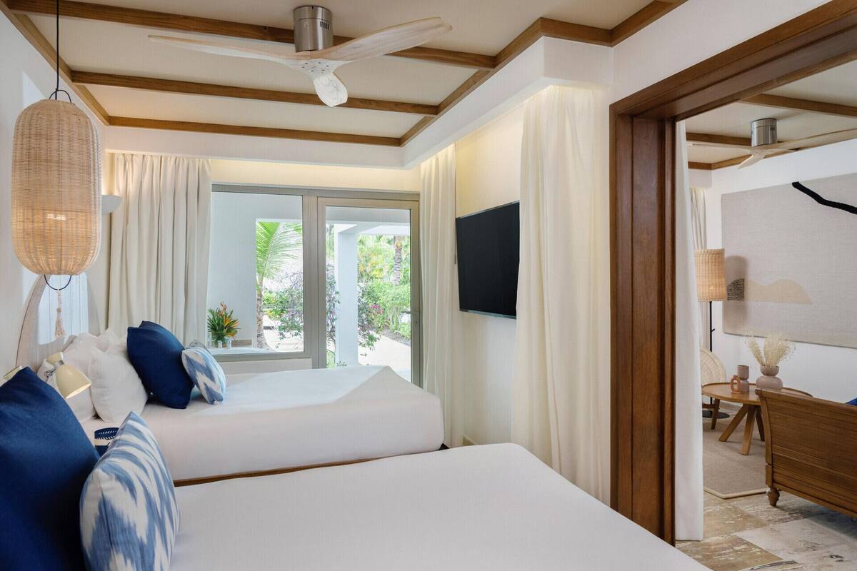 Habitación de hotel con dos camas, ventilador de techo, televisor y vista al exterior.