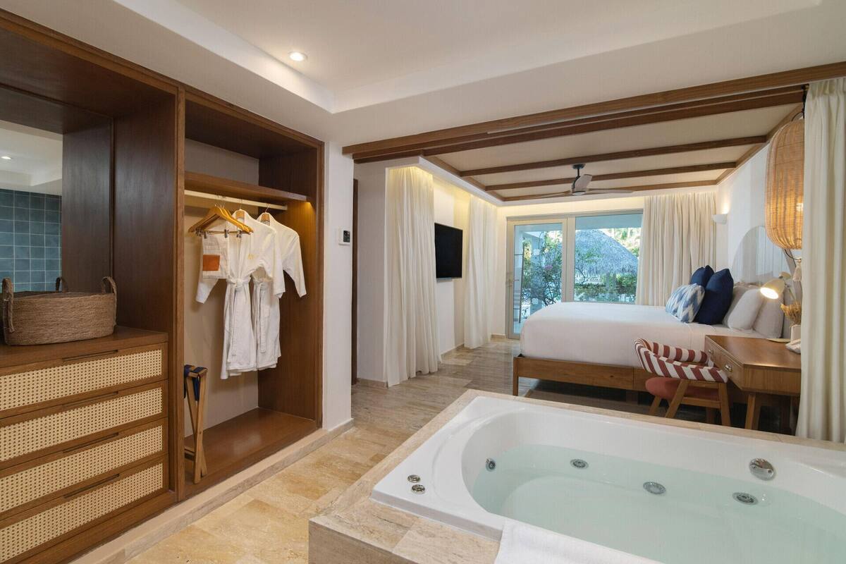 Habitación de hotel con una bañera grande, una cama con almohadas, un armario de madera y un televisor.