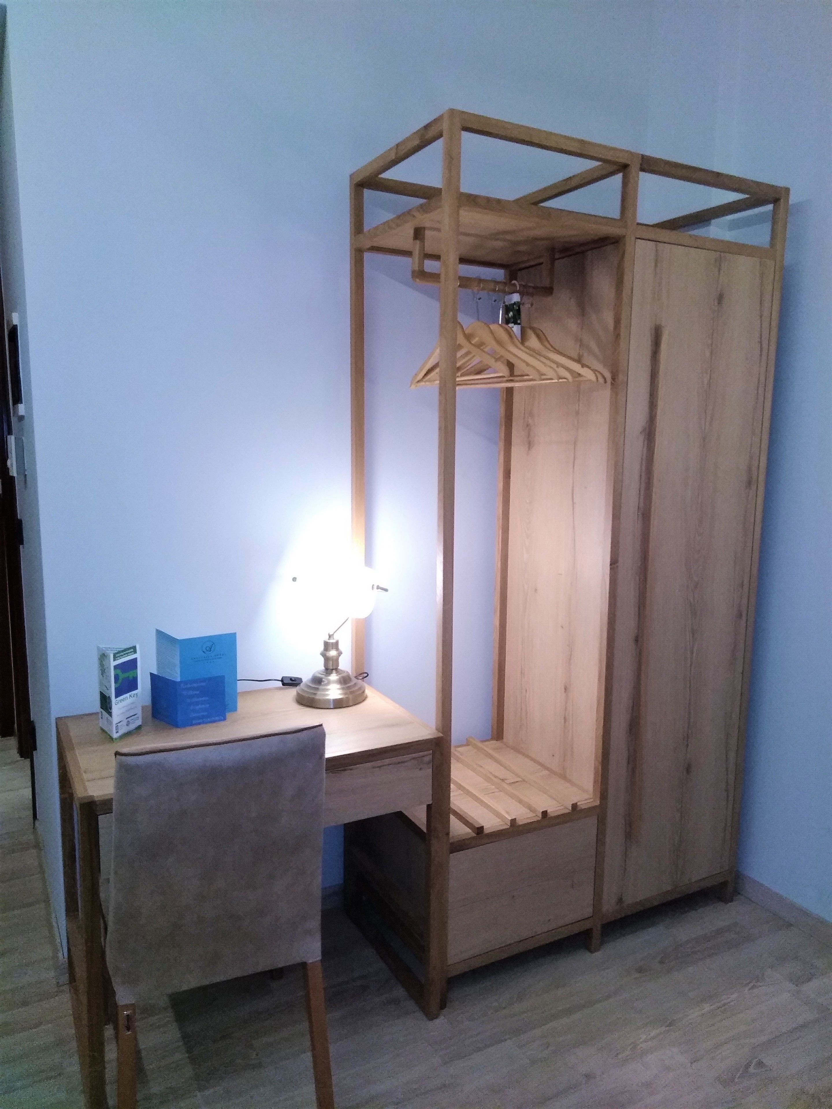 Um quarto pequeno de madeira com escrivaninha, cadeira e um cabideiro.