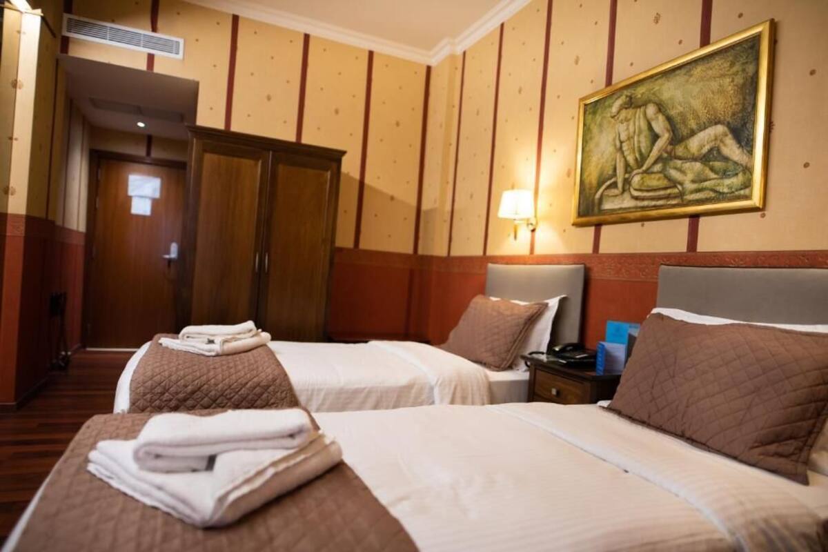 Una habitación de hotel con dos camas, un cuadro en la pared, una lámpara y un armario.