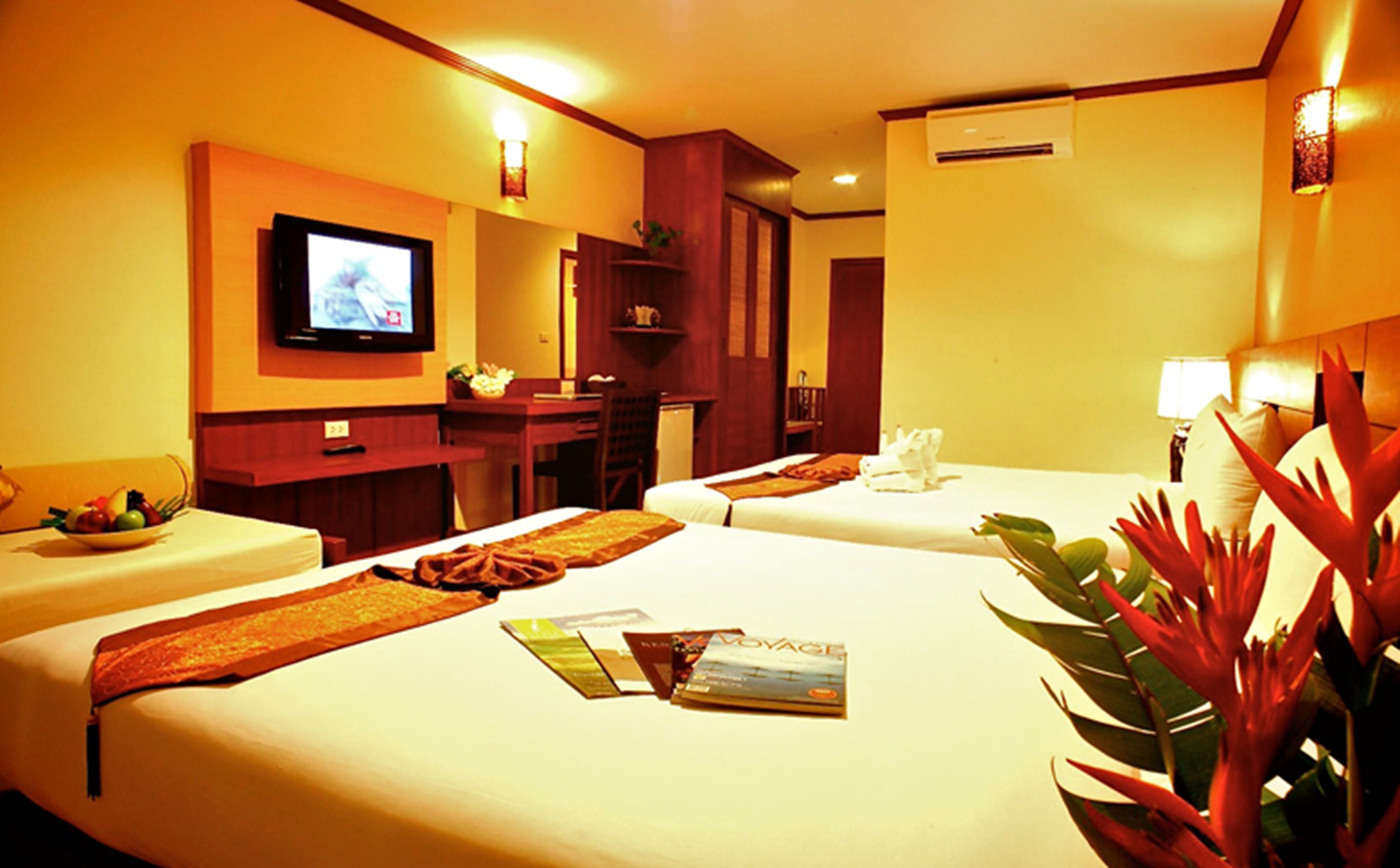 Habitación de hotel con dos camas, un escritorio, televisión y una planta.