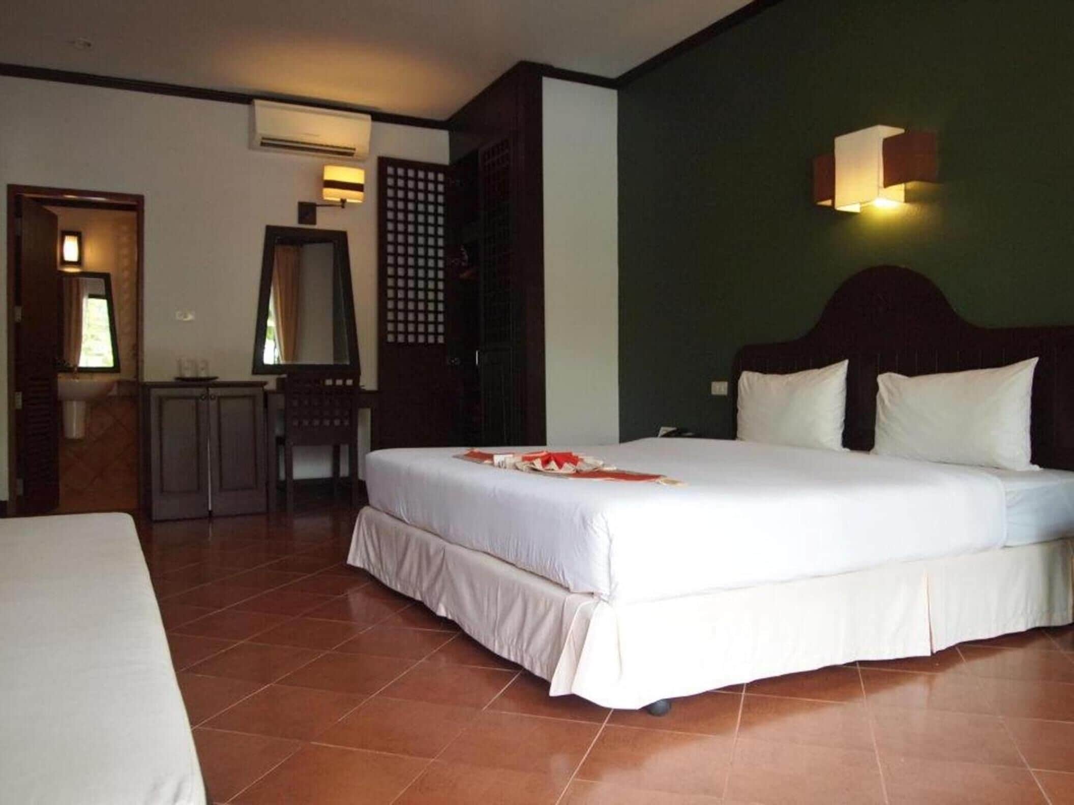 A hotel room with a large bed, a small desk, a mirror, and a wall-mounted light fixture.