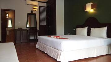 A hotel room with a large bed, a small desk, a mirror, and a wall-mounted light fixture.