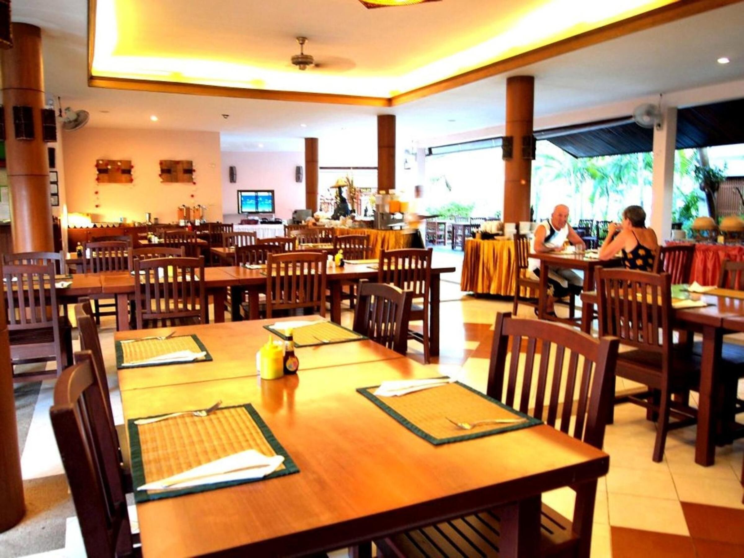 Un restaurante espacioso con mesas y sillas de madera, un ventilador de techo y vistas al exterior.