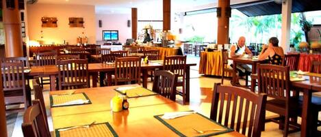 Un restaurante espacioso con mesas y sillas de madera, un ventilador de techo y vistas al exterior.