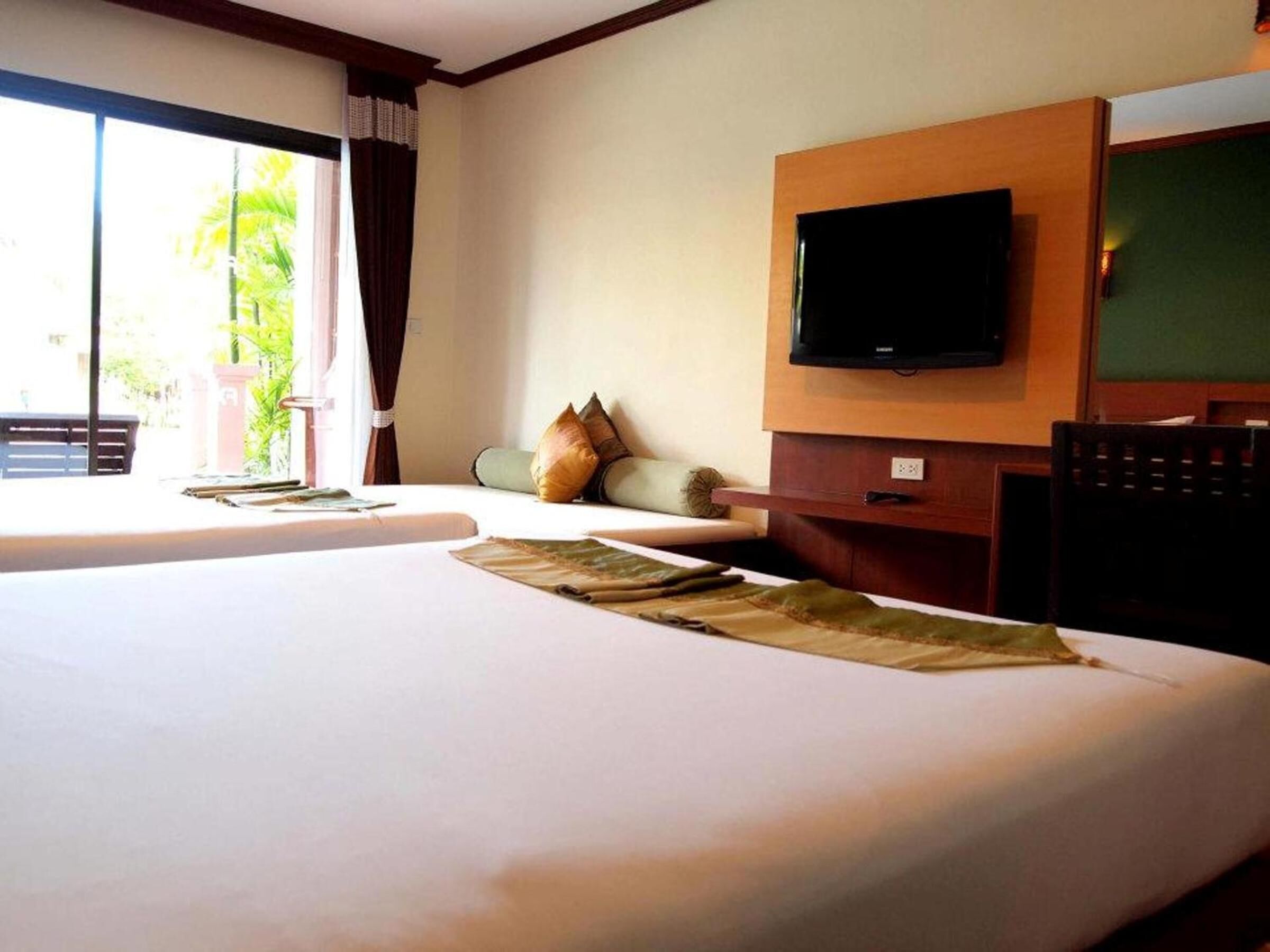 A hotel room with two beds, a flat-screen TV mounted on the wall, and a view of palm trees through the window.