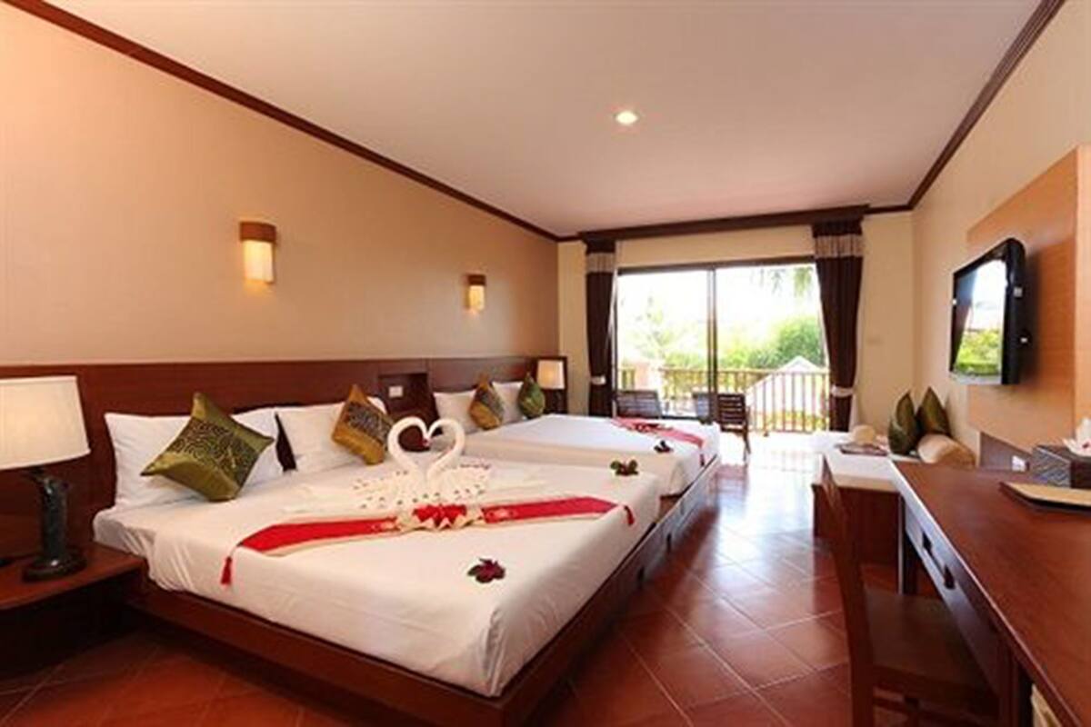 A hotel room with two beds, a TV, a desk, and a balcony with a view.