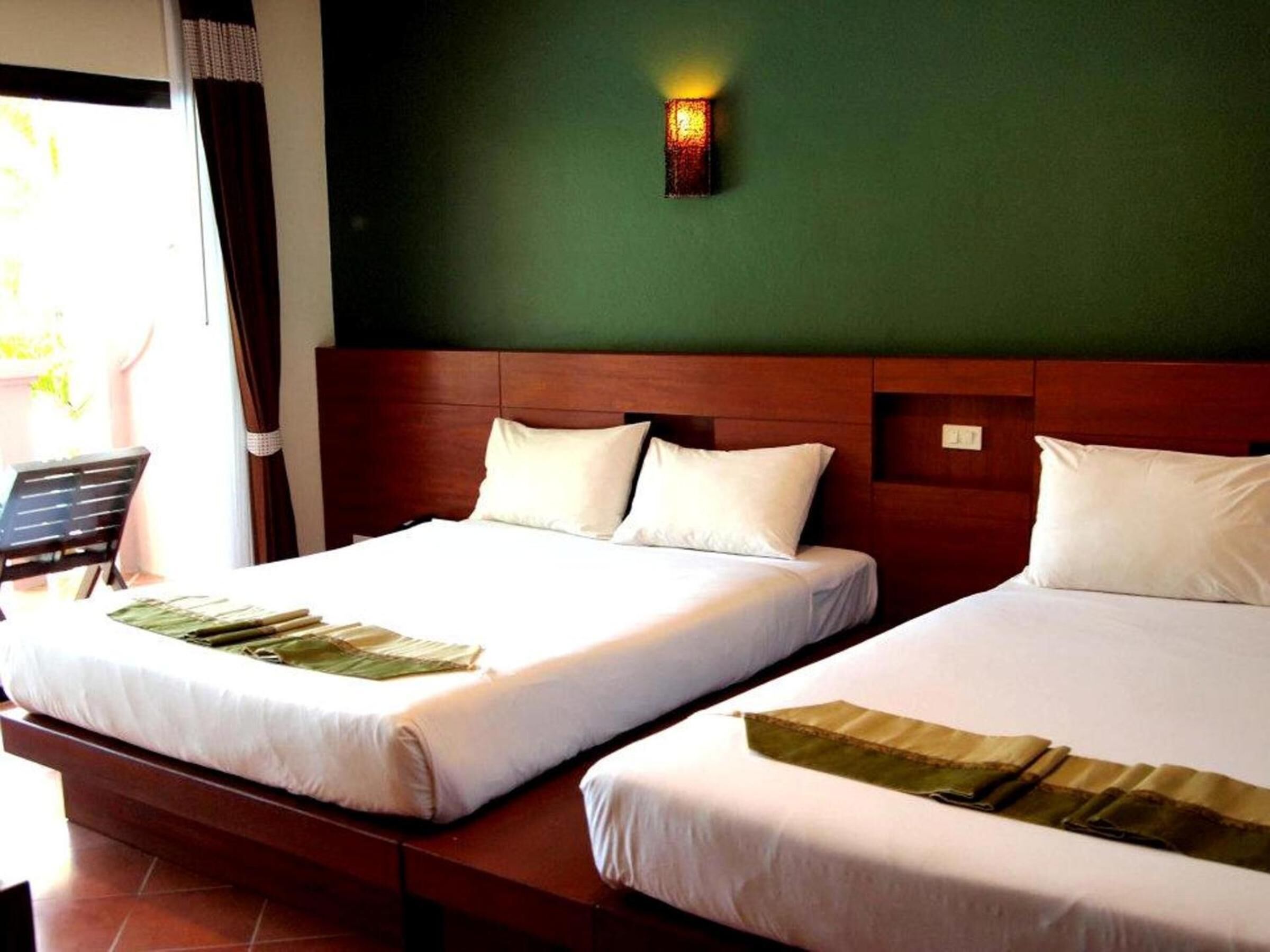 Une chambre d’hôtel avec deux lits, une tête de lit en bois et un luminaire fixé au mur.
