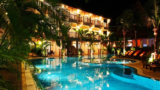 A nighttime view of a hotel with a large indoor swimming pool surrounded by palm trees and lounge chairs.