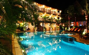A nighttime view of a hotel with a large indoor swimming pool surrounded by palm trees and lounge chairs.