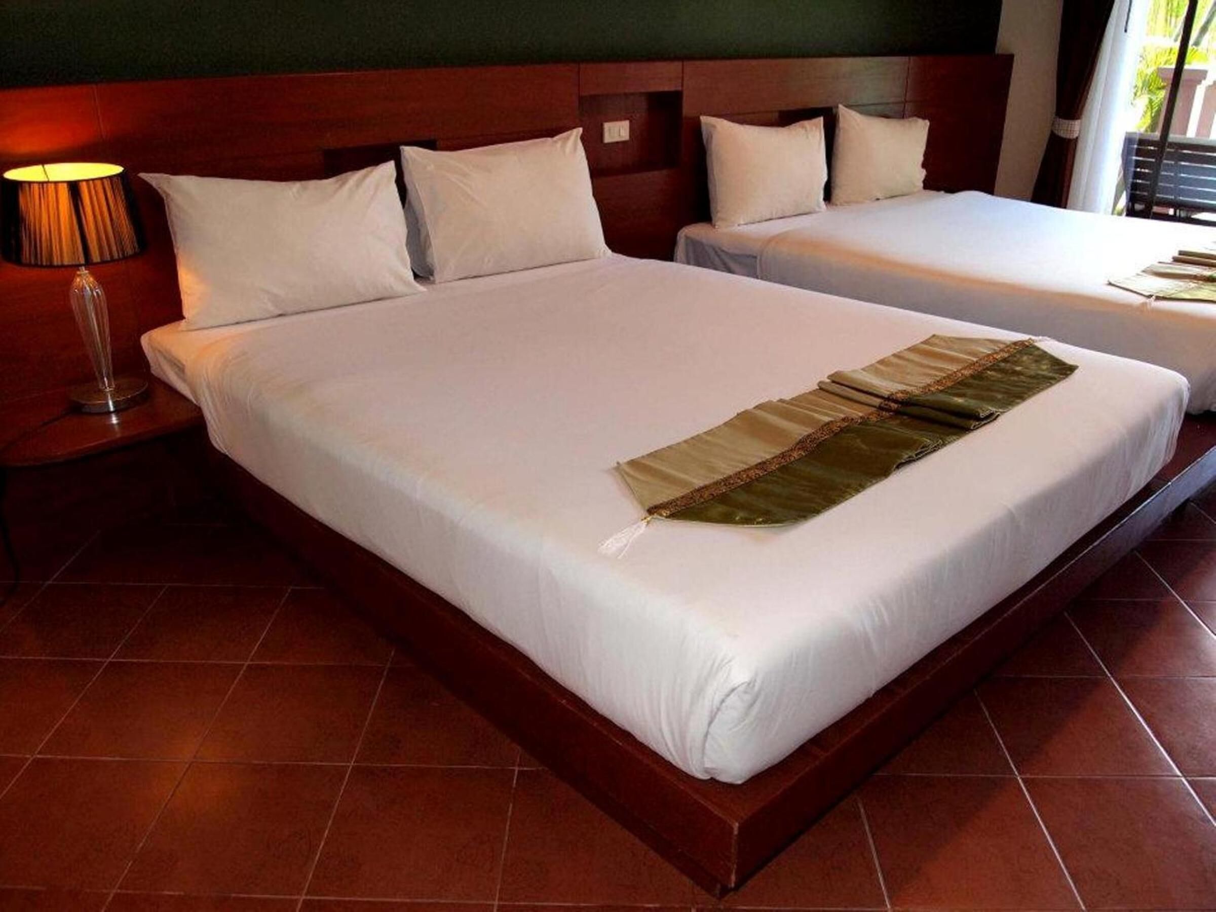 Habitación de hotel con dos camas, una mesita de noche con lámpara y vistas al exterior.