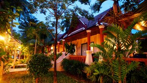 A tropical resort with a covered veranda, palm trees, and a staircase leading to the entrance.