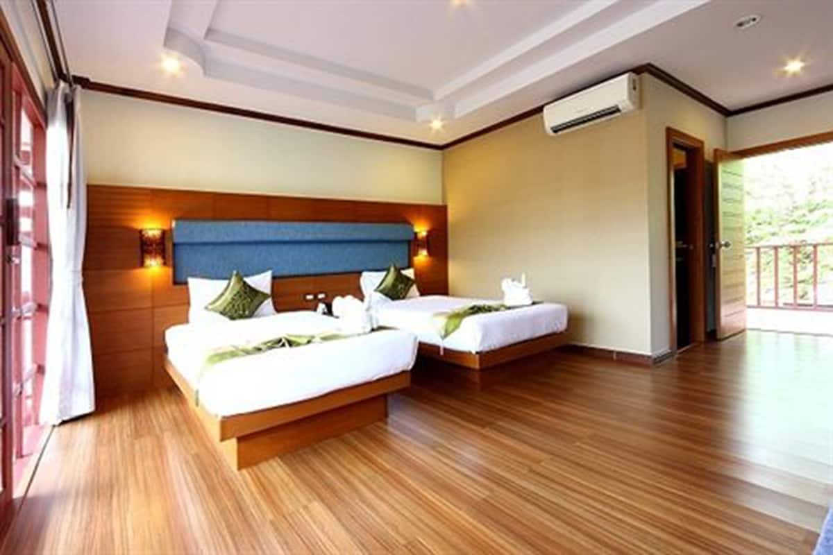 A hotel room with two beds, wooden flooring, a large window, and a door leading outside.