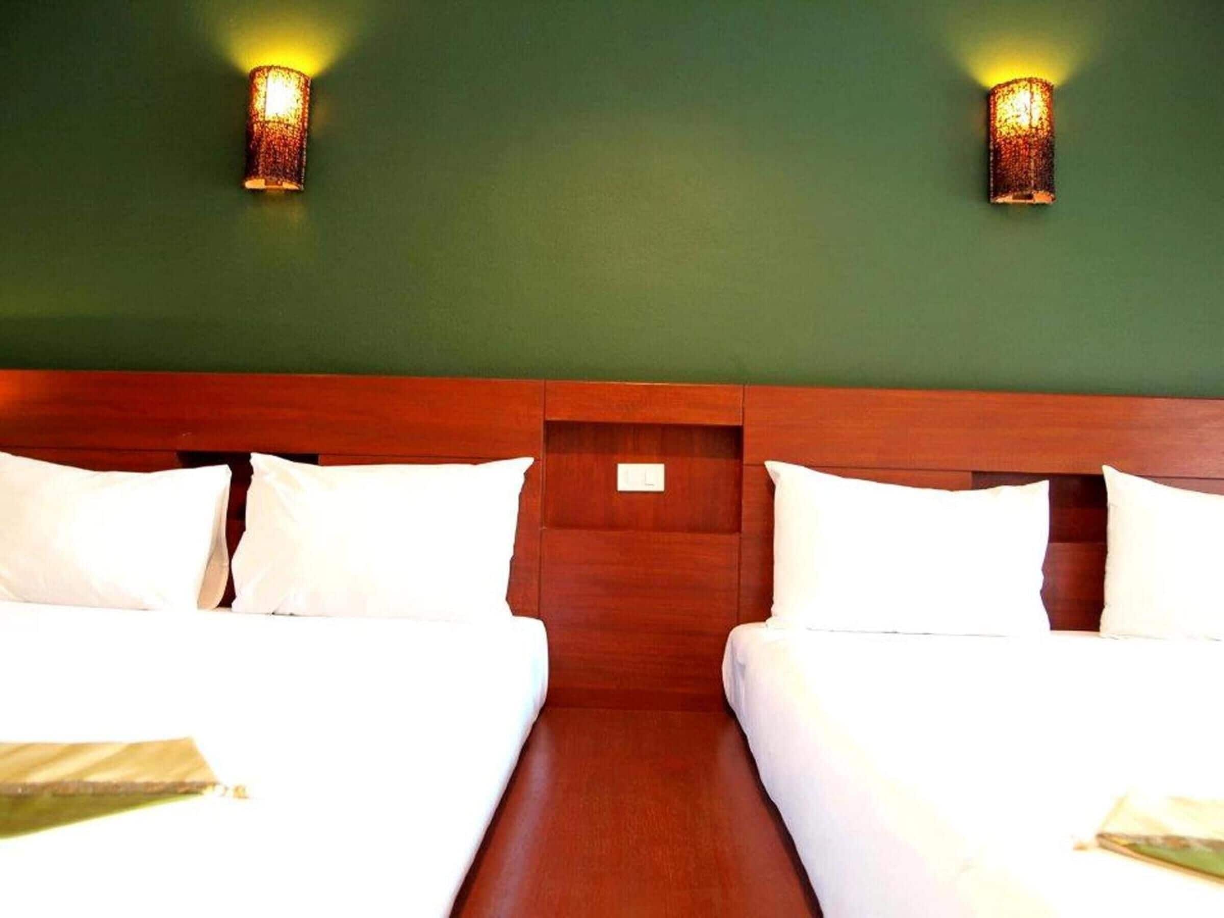 Una habitación de hotel con dos camas, un cabecero de madera y dos lámparas fijadas a la pared.