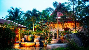 A traditional building with a red roof and a pond with rocks and plants.