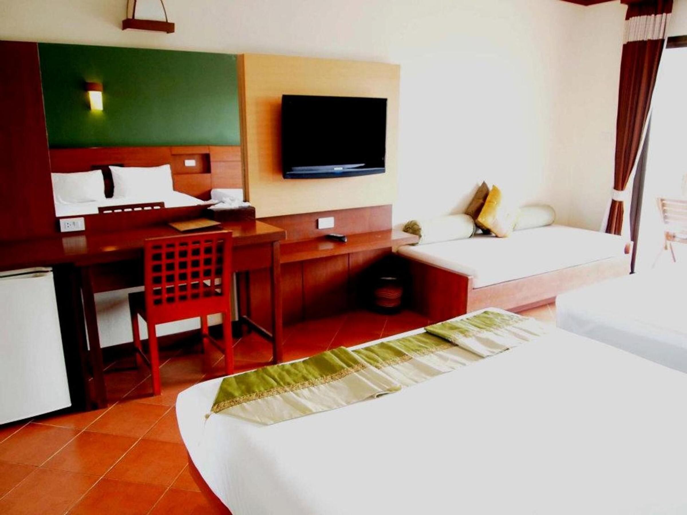 A hotel room with a bed, a desk, a chair, a television, and a sofa.