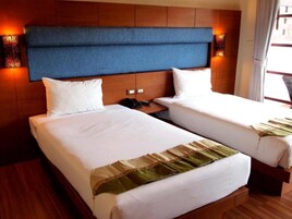 Habitación de hotel con dos camas, cabecero de madera, lámparas de noche y una ventana con cortinas.