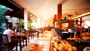 A restaurant with wooden tables and chairs, a buffet with pastries, and a view of the outdoors.