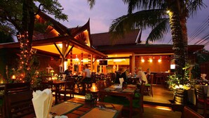 An outdoor restaurant with wooden tables and chairs, string lights, and a wooden deck.