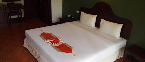 Una cama bien tendida con un cubreleche rojo y blanco decorativo, un cabecero de madera y una mesita de noche con una lámpara.