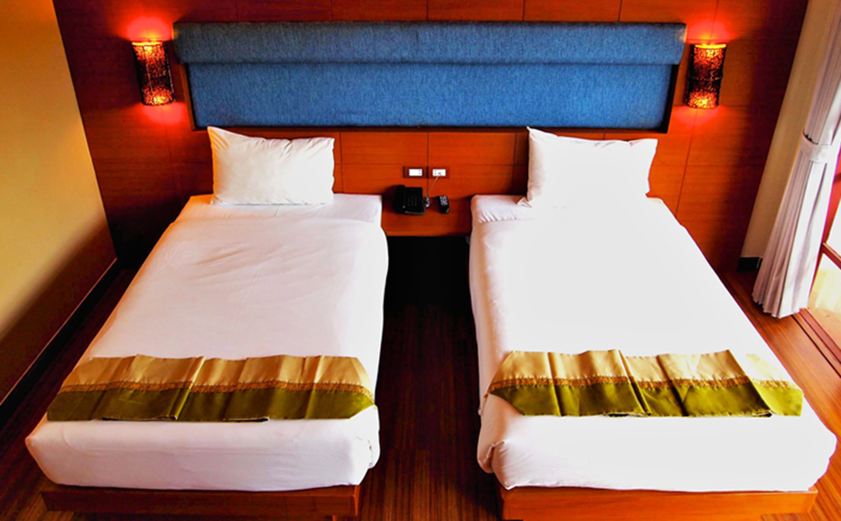 A hotel room with two single beds, a wooden headboard, bedside lamps, and a telephone on the nightstand.