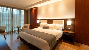 A hotel room with a large bed, bedside tables, a chair, a small table, and a window with curtains. - Hotel Ciudad De David (David)