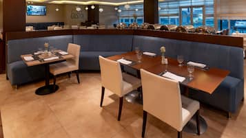 Un ristorante con interni moderni, che offre diverse disposizioni di posti a sedere, tra cui cabine e tavoli, e un'ampia vetrata con vista sulla strada.
