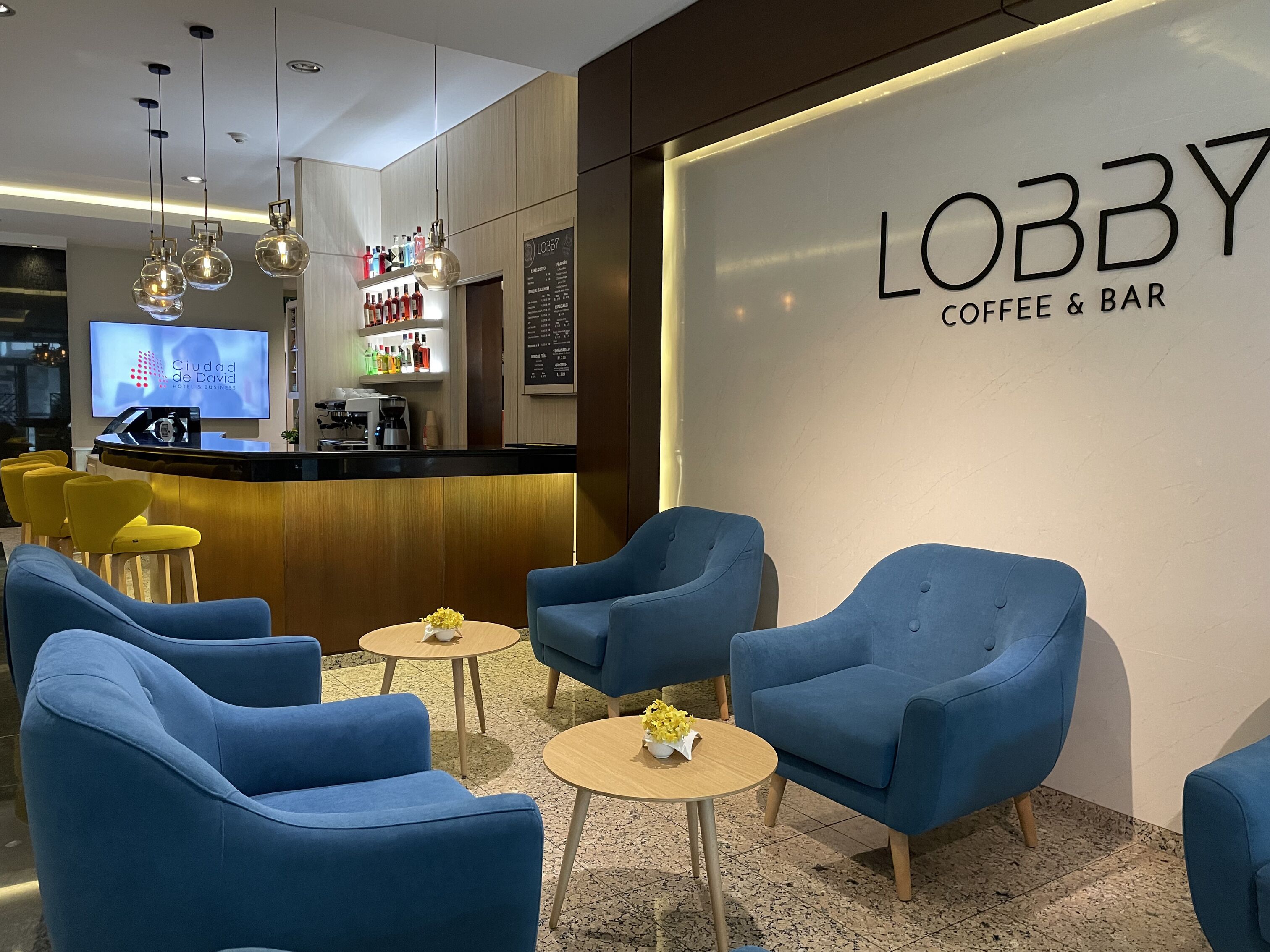 A lobby area with blue armchairs, a coffee bar, and a large screen displaying "LOBBY COFFEE & BAR".