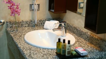 A bathroom with a granite countertop, a white sink, a towel, and a vase with pink flowers.