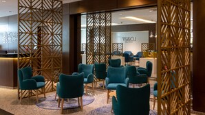 A modern hotel lobby with teal chairs arranged around a central table, a reception desk, and a decorative wooden partition. - Hotel Ciudad De David (David)