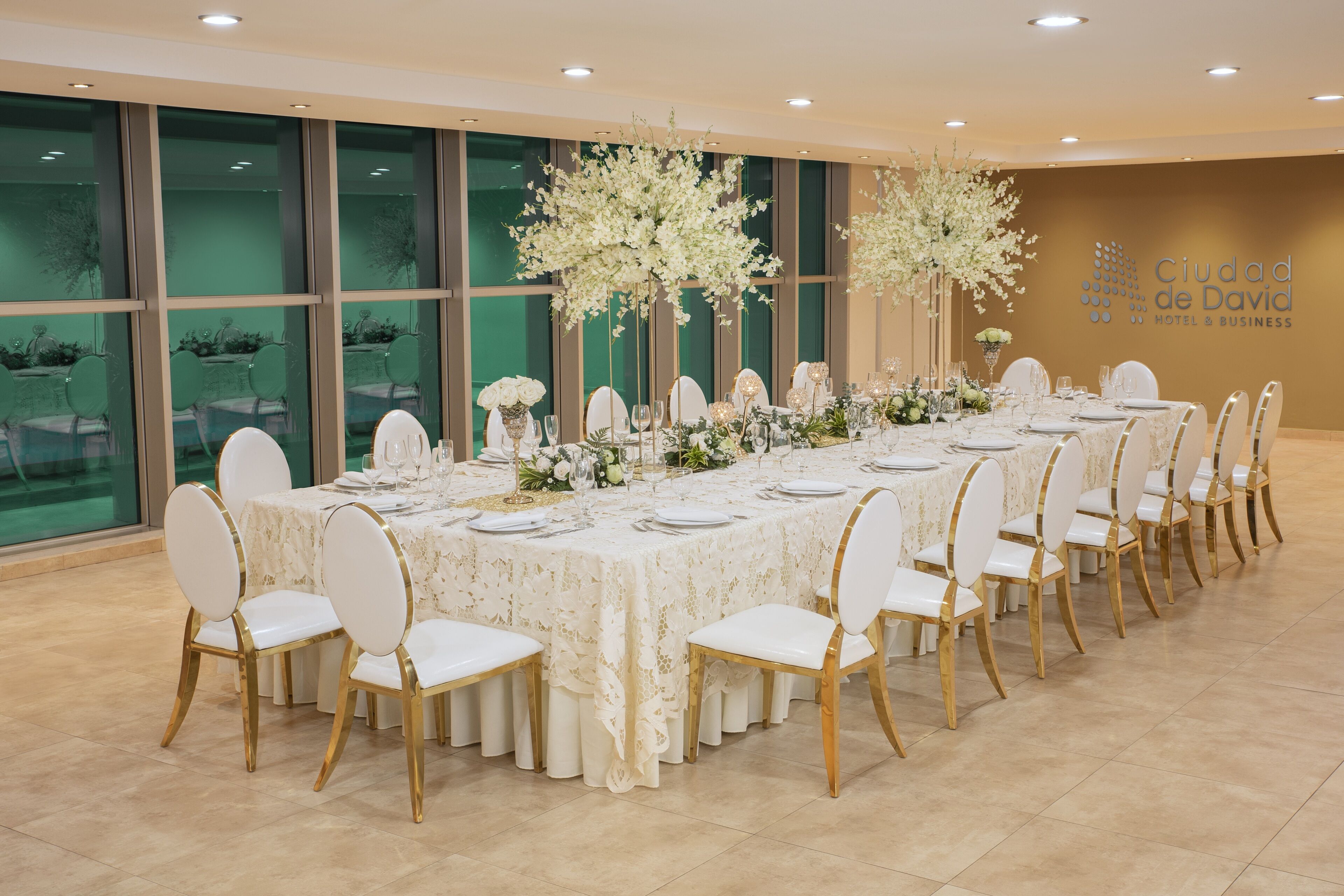 A banquet hall with a long table set for a formal event, surrounded by chairs with gold legs.