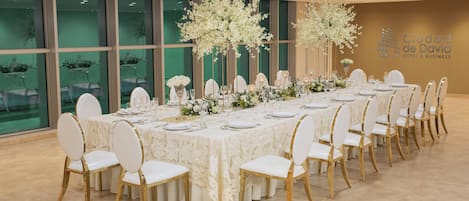 A banquet hall with a long table set for a formal event, surrounded by chairs with gold legs.