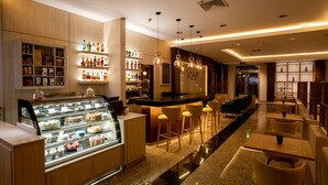 A modern bar area with a counter, stools, and a display case of desserts. - Hotel Ciudad De David (David)