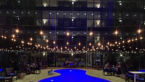 An indoor swimming pool with a blue tint, surrounded by seating areas and potted plants. - Hotel Ciudad De David (David)